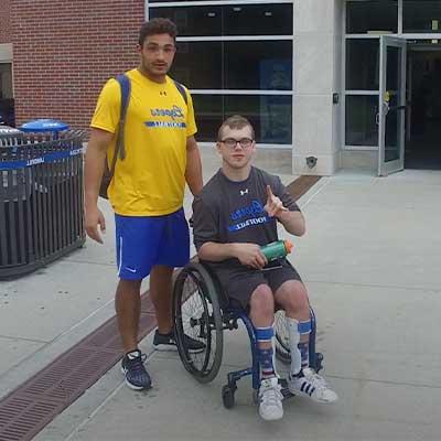 a student stands next to a student using a wheelchair throwing the lopes